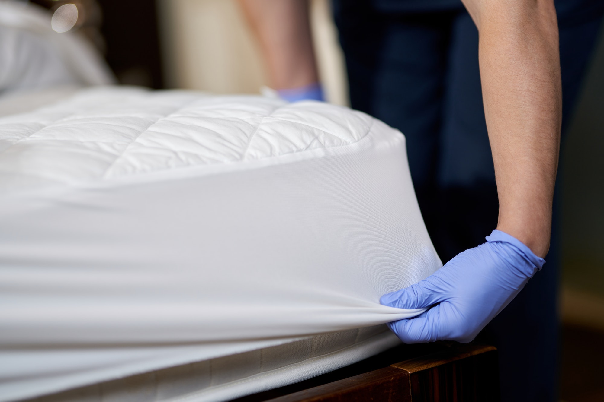 Housekeeper in gloves changing bedding in hotel room